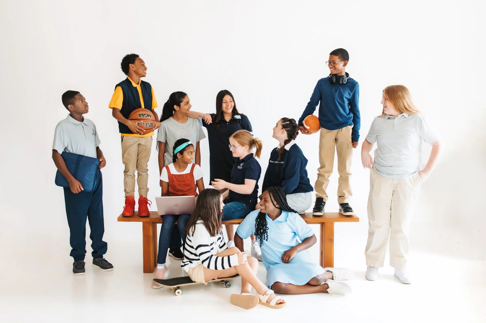 A large group of Way Christian Academy students gathered together with sports equipment, books, and a laptop in a bright studio